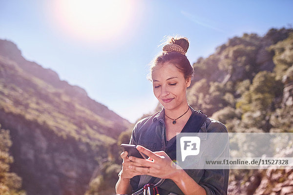 Junge Frau SMS mit Handy unter sonnigen Klippen