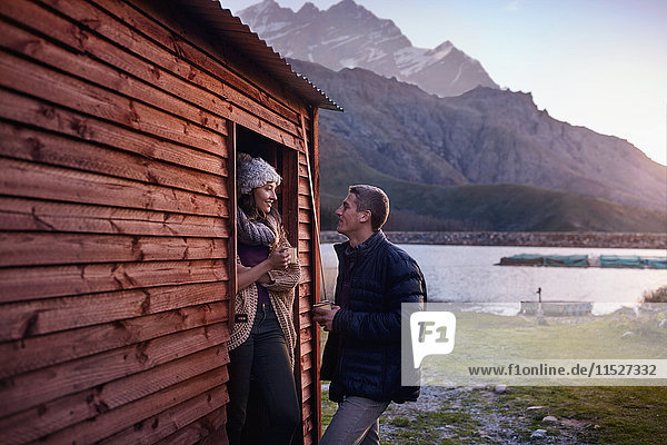 Young couple drinking coffee at lakeside cabin doorway