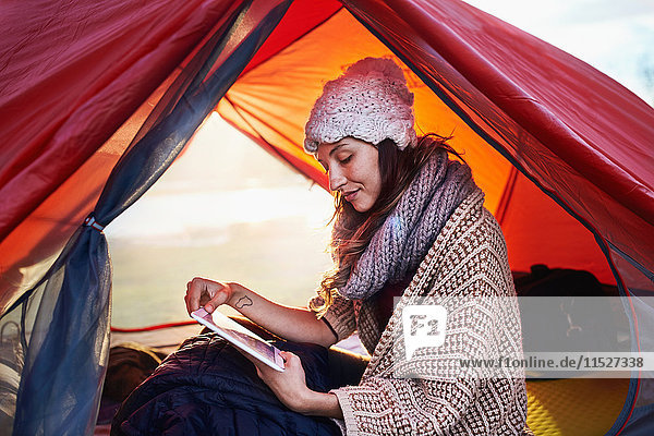 Junge Frau beim Zelten  mit digitalem Tablett im Zelt