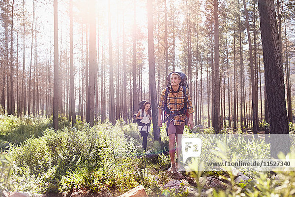 Junges Paar mit Rucksäcken beim Wandern in sonnigen Wäldern