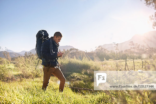 Young man with backpack hiking  checking compass in sunny  remote field