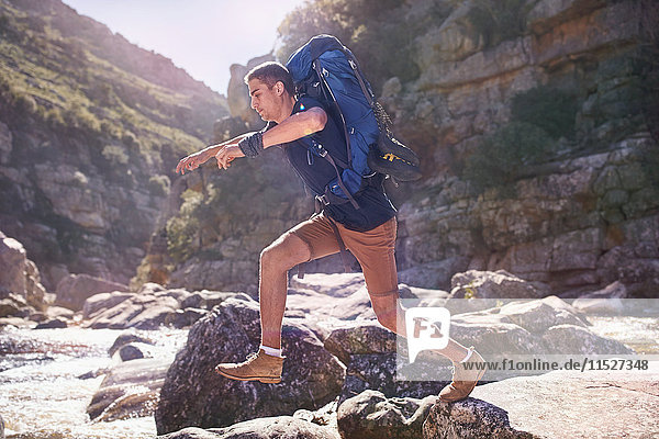 Young man with backpack hiking  jumping rocks