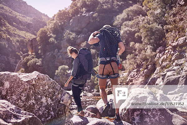 Young couple with backpacks hiking over sunny rocks