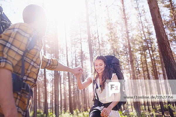 Junger Mann hilft Freundin beim Rucksackwandern im sonnigen Wald