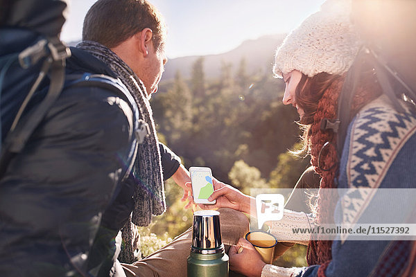 Young couple hiking  taking a coffee break and using smart phone