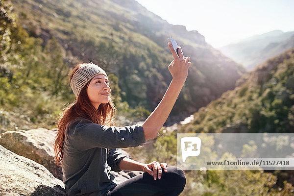 Young woman taking selfie with camera phone on sunny  remote rock
