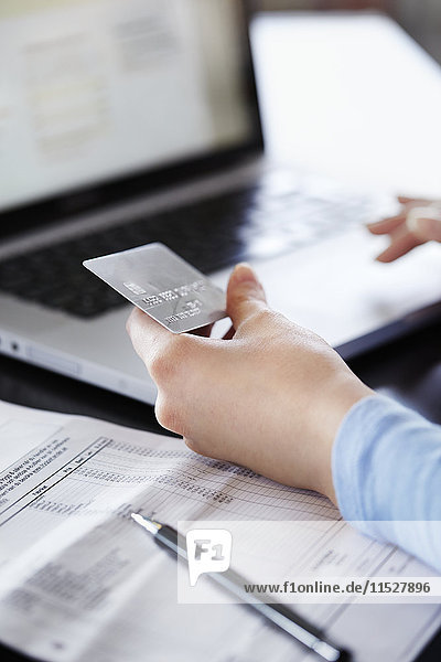 Frau hält Kreditkarte und benutzt Laptop