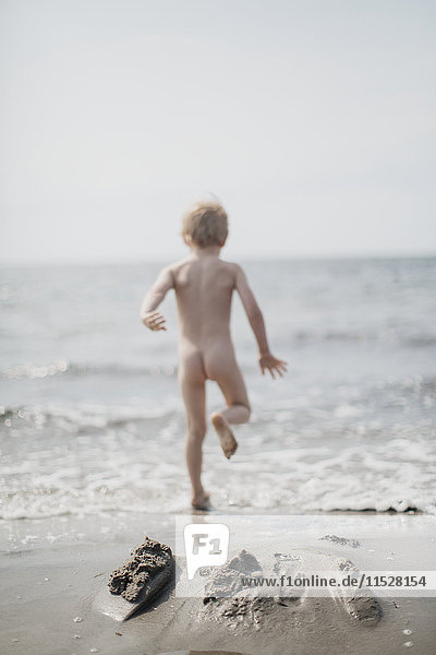 Nude boy running into sea