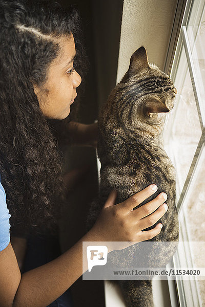 Ein junges Mädchen mit einer Katze am Fenster.