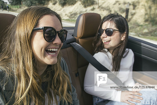 Zwei Frauen mit Sonnenbrille lachend in einem Cabriolet