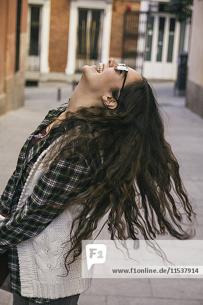 Lachende junge Frau mit langen braunen Haaren und Sonnenbrille