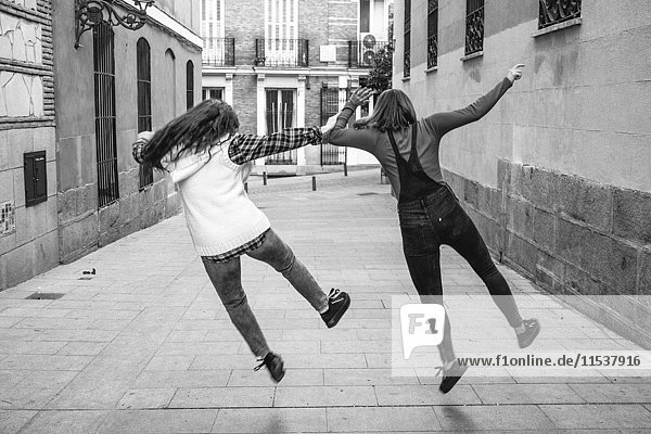Spanien  Madrid  Rückansicht von zwei jungen Frauen beim Springen auf der Straße