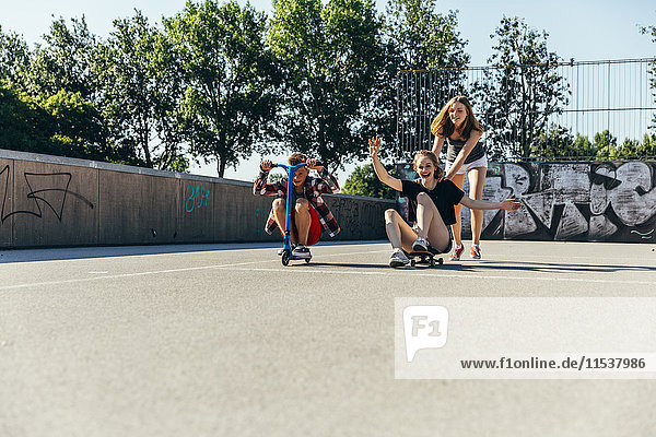 Three playful teenage friends with scooter and skateboard