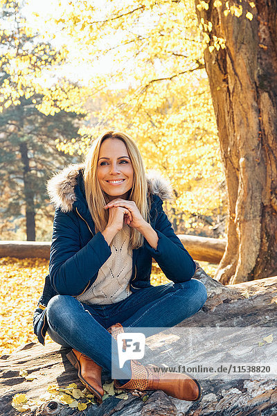 Smiling woman enjoying autumn in a forest sitting on a trunk