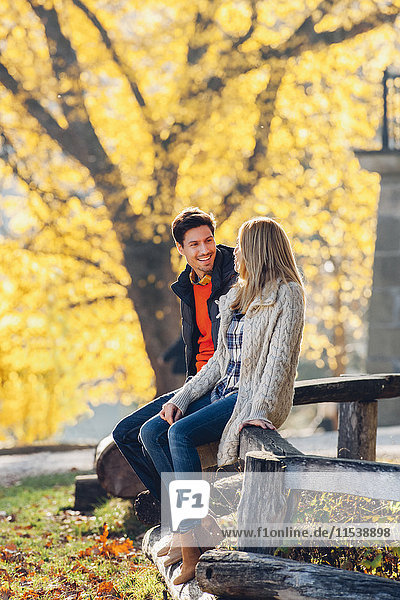 Glückliches Paar sitzt auf Holzgeländer im herbstlichen Park