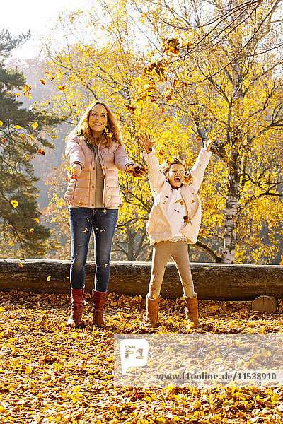 Mother and her little daughter throwing autumn leaves into the air