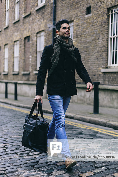 Young casual businessman walking in the street  carrying bag