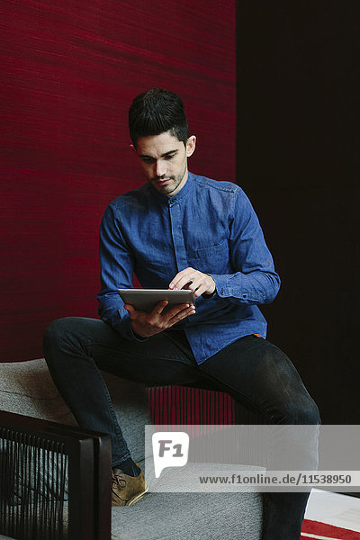 Junger Geschäftsmann sitzt auf dem Sessel einer Lobby mit seinem digitalen Tablett