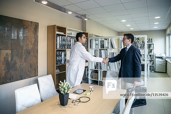 Mann im Anzug und Arzt beim Händeschütteln in der Praxis