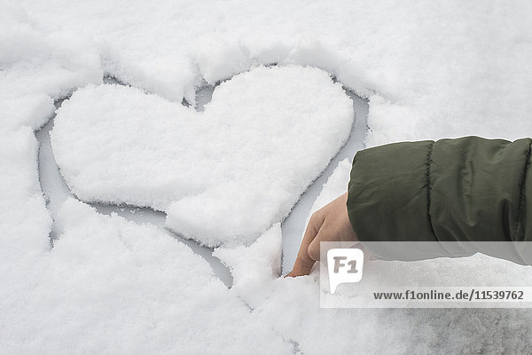Finger eines kleinen Jungen  der ein Herz im Schnee auf einem Auto schnitzt.