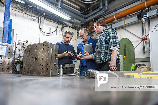 Three men in factory discussing workpieces