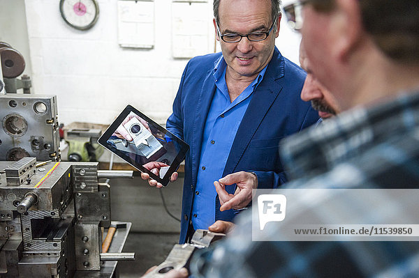 Drei Männer mit digitalem Tablett diskutieren über ein Werkstück