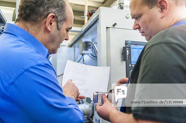 Two men discussing a metal workpiece