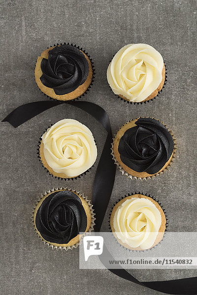 Sechs Tassen Kuchen mit schwarzer und cremefarbener Buttercreme und schwarzem Band