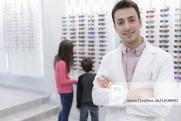Porträt eines lächelnden Optikers im Geschäft mit Menschen im Hintergrund