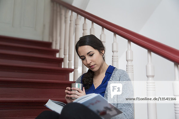 Frau im Treppenhaus mit Kaffee und Lesebuch