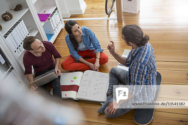 Drei kreative Geschäftsleute  die auf dem Boden sitzen und diskutieren