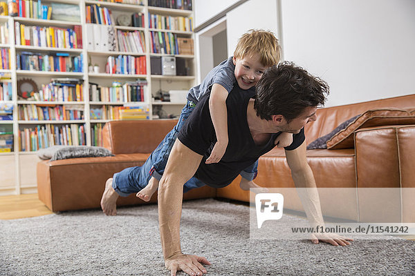 Father doing push ups in living room with son on his back