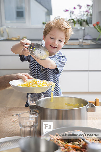 Proud little boy serving pasta in kitchen