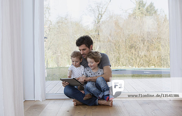 Vater und Söhne sitzen auf dem Boden und benutzen ein digitales Tablett.