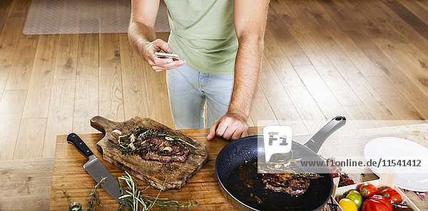 Man with prepared steaks in kitchen using celll phone