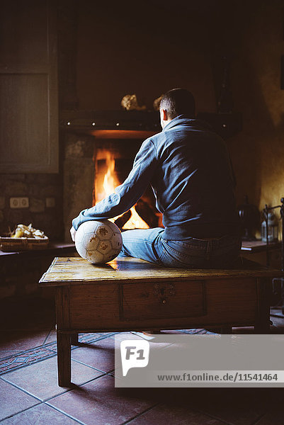 Mann sitzt vor dem Kamin mit einem Fußballball