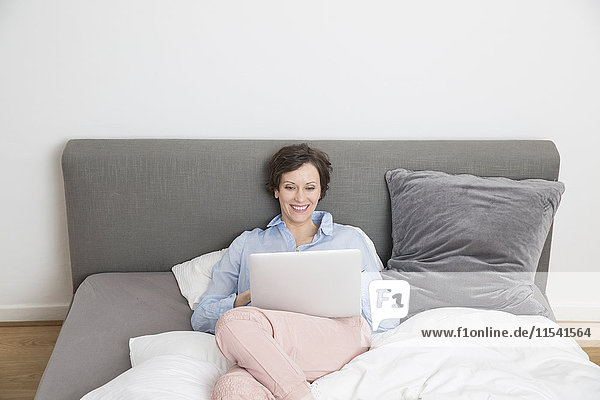 Glückliche Frau auf dem Bett liegend mit Laptop