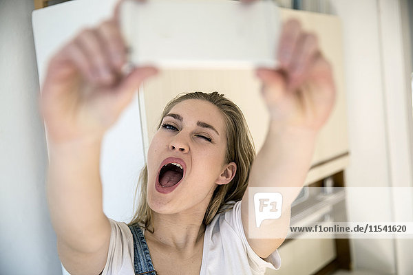 Porträt einer jungen Frau  die den Mund schmollt  während sie sich selbst mit dem Smartphone nimmt.