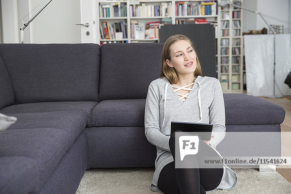 Junge Frau sitzt auf dem Boden des Wohnzimmers mit digitalem Tablett