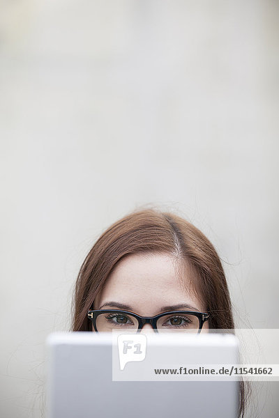 Junge Frau mit Brille  die sich hinter einem digitalen Tablett versteckt.