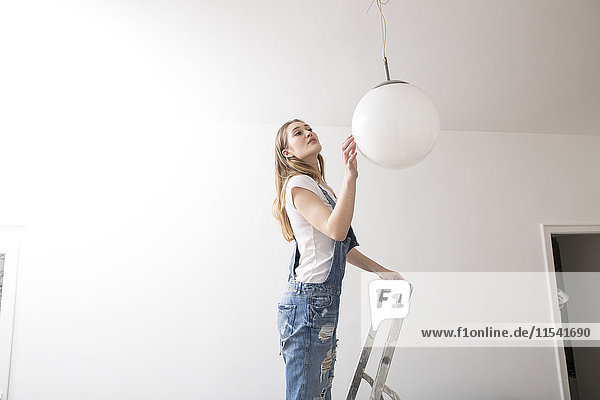 Young woman standing on a ladder checking ceiling light