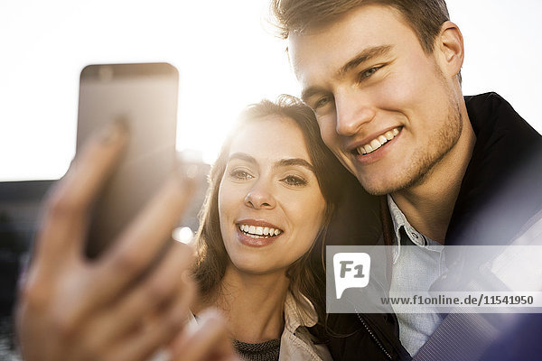 Lächelndes junges Paar mit einem Selfie im Freien