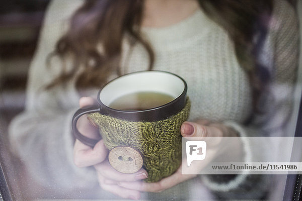 Junge Frau am Fenster stehend mit einer Tasse Tee