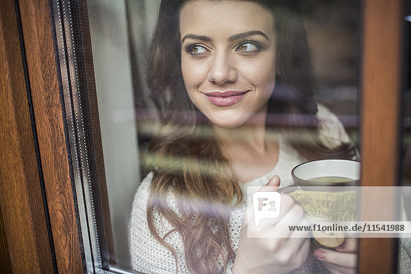 Junge Frau am Fenster stehend mit einer Tasse Kaffee