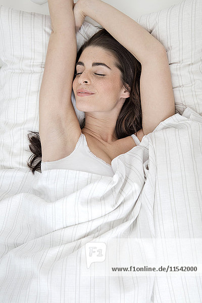 Lächelnde junge Frau schläft im Bett