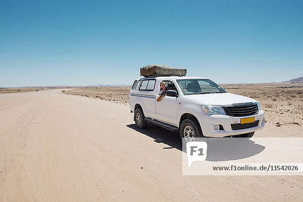 Namibia  Namib Wüste  Swakopmund  Mann auf einem 4x4 Auto mit Zelt auf dem Dach in einer staubigen Straße