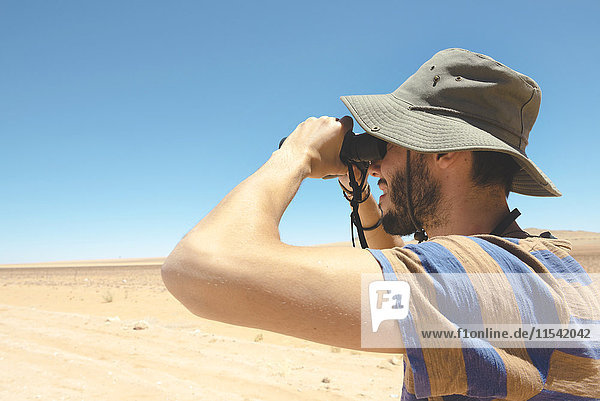 Namibia  Namib Wüste  Mann mit Hut mit Fernglas zum Wegschauen