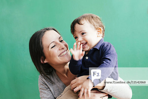 Porträt der glücklichen Mutter mit ihrem kleinen Sohn vor grünem Hintergrund