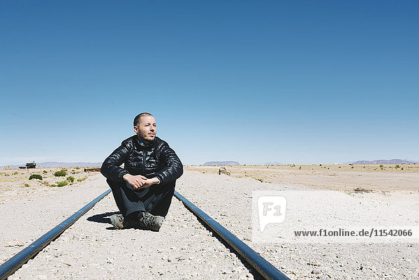 Bolivien  Uyuni-Zugfriedhof  Mann auf der Eisenbahn sitzend und weit weg schauend
