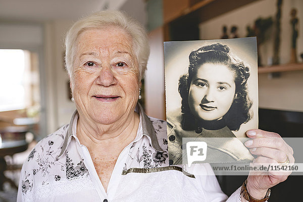 Portrait of senior woman showing an old picture of herself